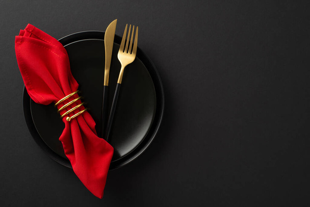 Black Friday grandeur : vue de dessus décor de table haut de gamme avec des essentiels gastronomiques, plats, couverts, serviette rouge en anneau d'or sur fond noir élégant. Idéal pour la publicité de vos offres spéciales - Photo, image