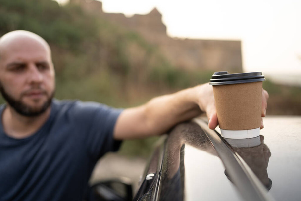 Ο οδηγός βάζει ένα φλιτζάνι καφέ στην οροφή του αυτοκινήτου. Άνθρωποι όχημα και τον τρόπο ζωής έννοια - Φωτογραφία, εικόνα