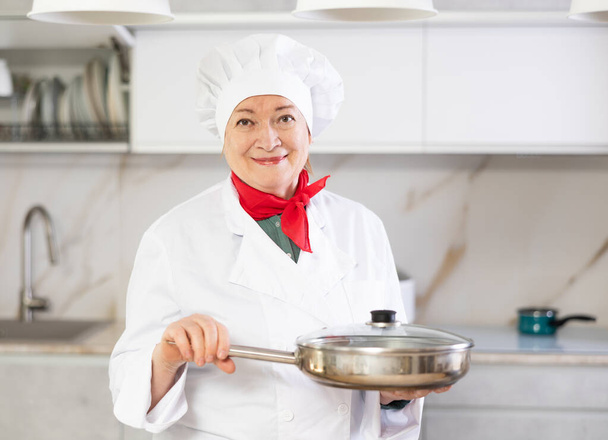 Confident mature woman in cook outfit showing around hew kitchen - Foto, Bild