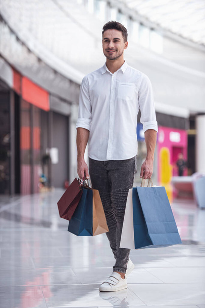 Retrato de cuerpo entero de chico guapo con bolsas de compras sonriendo mientras hace compras en el centro comercial
 - Foto, imagen