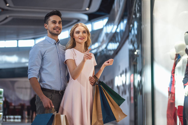 Bella coppia con borse della spesa sta parlando e sorridendo mentre fa shopping nel centro commerciale
 - Foto, immagini