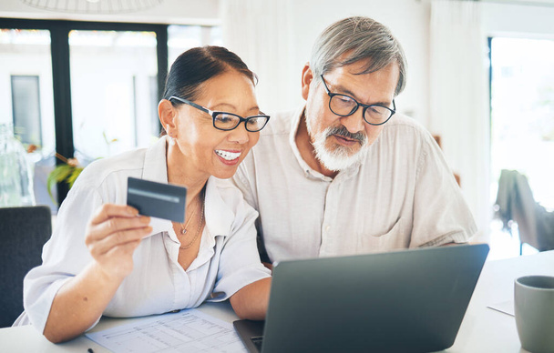 Mature couple, credit card and computer for home online shopping, loan application or digital money or finance in kitchen. Happy woman and man on laptop internet banking, easy payment or registration. - Photo, Image