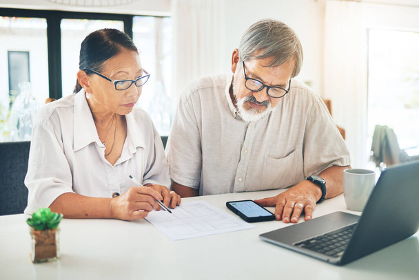 Senior couple, phone and finance in budget planning, invoice or documents together on table at home. Mature man and woman writing in financial plan, expenses or bills with paperwork on desk at house. - Photo, Image