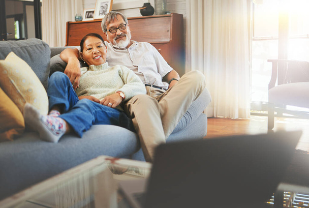 Старшая пара смотрит фильм на диване с ноутбуком в гостиной вместе для сближения. Счастливые, улыбчивые и пожилые мужчины и женщины на пенсии расслабляются и показывают или снимают кино в домашних условиях - Фото, изображение