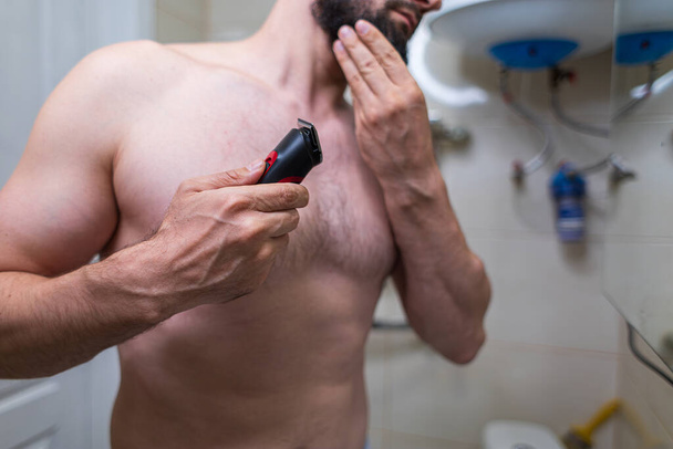 Een man maakt zich klaar om zich te scheren met een krachtig weefgetouw. Een man met een atletische figuur in de badkamer. - Foto, afbeelding