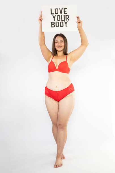 Portret van zelfminnende vrouw plus size in rood ondergoed op witte achtergrond, body love - Foto, afbeelding