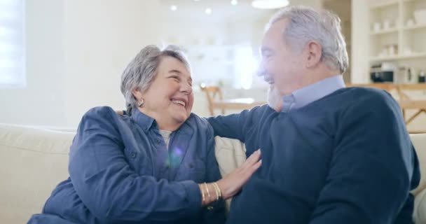 Mature, man and woman with joke in home on sofa in living room, together and bond. Elderly couple, smile and laugh in happiness with touch, humor and fun for relationship with love in retirement. - Footage, Video