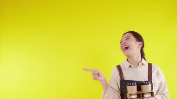 Retrato jovem asiático barista mulher vestindo avental segurando xícara de café e apresentando no fundo amarelo, garçonete ou empreendedor alegre e mostrando e polegares para cima, pequenas empresas ou startup. - Filmagem, Vídeo