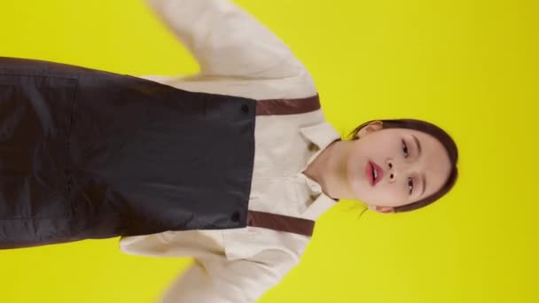 Portrait of young asian barista woman wearing apron standing and unhappy gesture dislike on yellow background, waitress or entrepreneur disappointed, small business or startup with failure. - Footage, Video