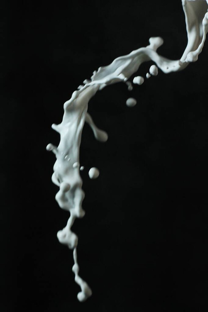 salpicadura de líquido negro en forma de leche sobre un fondo negro - Foto, imagen
