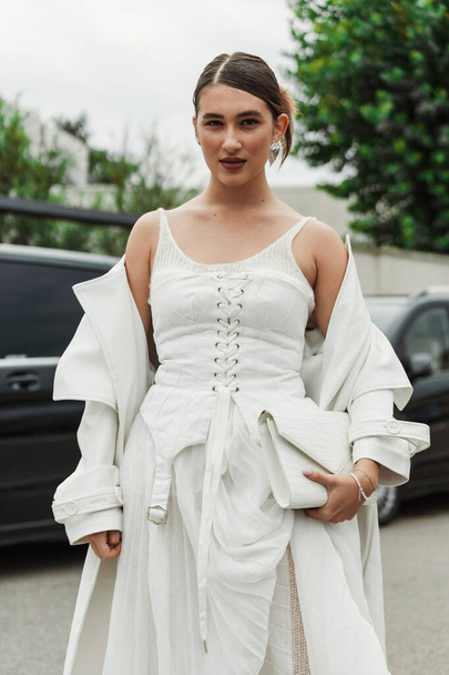 Ένας επισκέπτης φοράει λευκό φόρεμα, παλτό και τσάντα, δει έξω από την επίδειξη PRADA κατά τη διάρκεια της εβδομάδας μόδας του Μιλάνου Γυναικεία ενδύματα Άνοιξη / Καλοκαίρι 2024. - Φωτογραφία, εικόνα