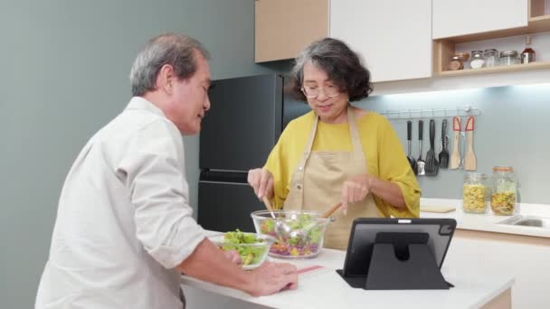 Азиатская старшая пара смотреть рецепт с планшетом делает салат овощ вместе на кухне дома, семья с пожилыми готовит салат к обеду с удовлетворением, сближение и отношения. - Кадры, видео