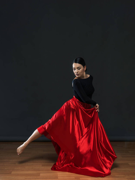 Χορευτής με κόκκινη φούστα. Γυναίκα χορεύτρια με μαύρο κοστούμι σε γκρι φόντο. - Φωτογραφία, εικόνα