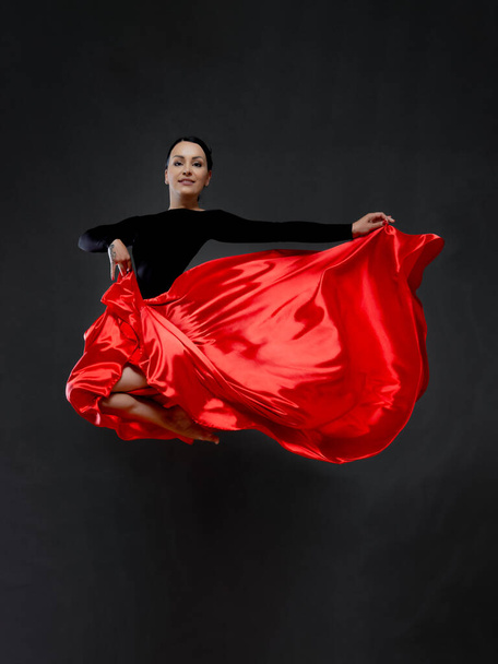Bailarina con una falda roja brillante. Bailarina femenina en un body negro sobre fondo gris. - Foto, Imagen