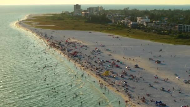 アメリカのサラソータ州の観光客でいっぱいの白い砂と夕方のシエスタキービーチの上からの眺め. 暖かいフロリダの日差しで水泳とリラックスで休暇時間を楽しむ多くの人々. - 映像、動画