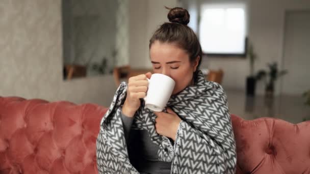 Beteg nő ül a kanapén a meleg takaró alatt, köhög, erős fejfájás, láz és forró teát iszik otthon. Az egészségtelen nőnek influenzavírus tünetei vannak, lassított felvétel. - Felvétel, videó