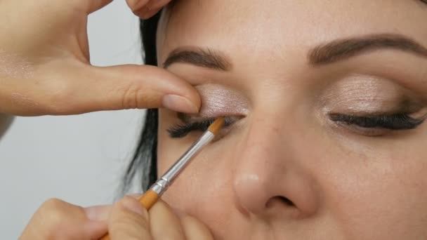 Een mooie jonge vrouw doet stijlvolle avond make-up door een professionele make-up kunstenaar in een beauty studio met behulp van een speciale borstel om oog make-up te doen.. - Video