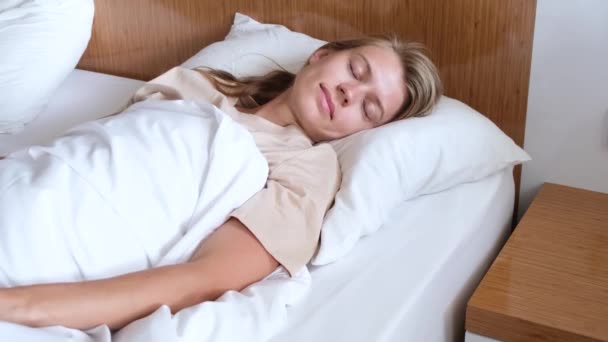 Νεαρή γυναίκα ξυπνά και τεντώνεται το πρωί στο δωμάτιο του ξενοδοχείου - Πλάνα, βίντεο