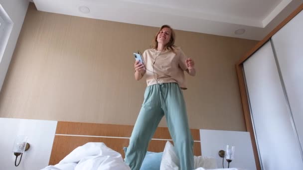 Jonge vrouw dansend op het bed in hotelkamer, genietend van haar vakantie - Video