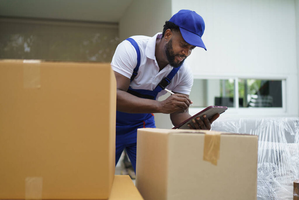 Afrikanischer Kurier Mann Haus Mover Überprüfung Karton vor dem Umzug zum Kunden. - Foto, Bild