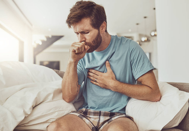 Sick, coughing and man on a sofa with chest pain, tuberculosis or influenza at home. Asthma, anxiety and male person with breathing trouble in living room with covid, pneumonia or lung virus. - Photo, Image