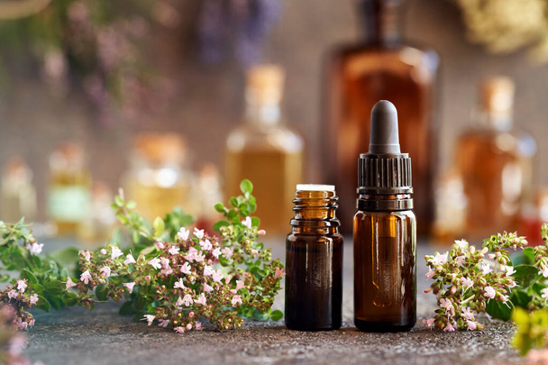 Brown bottles of aromatherapy essential oil with fresh oregano leaves and flowers on a table - Photo, Image
