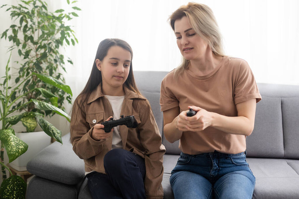 Familia feliz juntos. Madre y su hija jugando videojuegos. Gente divirtiéndose en casa
. - Foto, imagen