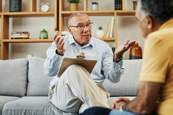 Senior man spreekt met een psycholoog bij geestelijke gezondheid, psychologie en therapie kliniek voor sessie. Psychologische therapeut met klembord voor counseling checklist met oudere mannelijke patiënt in het kantoor - Foto, afbeelding