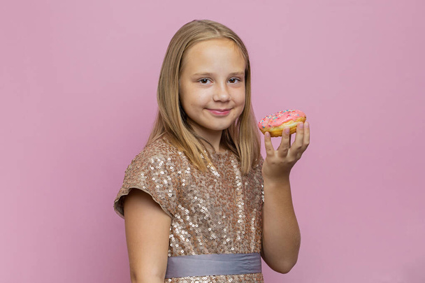 Красивая маленькая девочка ест розовый пончик на красочном розовом фоне с копировальным пространством - Фото, изображение