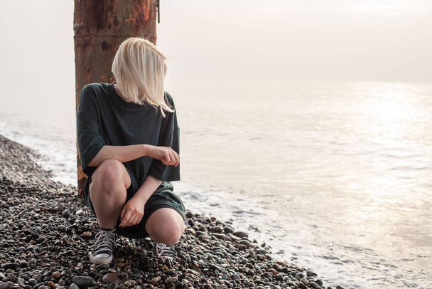 Jovem mulher casual com cabelo loiro sentado na praia do mar - Foto, Imagem