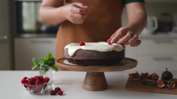 Jovem atraente cozinhar na cozinha. Vídeo cortado de atraente jovem decorando bolo de chocolate tradicional com esmalte e bagas na cozinha, foco na mão - Filmagem, Vídeo