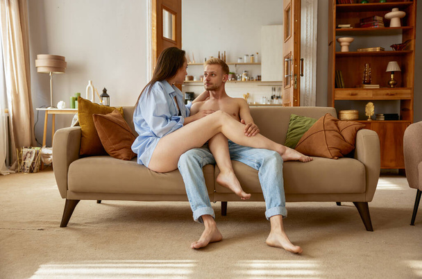 Hermosa mujer sensual y hombre sexy hablando juntos sentados en el sofá. Sexy novia apasionada y novio en casa - Foto, imagen