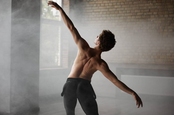 Bellissimo ballerino di balletto uomo senza camicia che fa elemento di danza sullo sfondo dello studio. Moderna formazione coreografa al chiuso - Foto, immagini