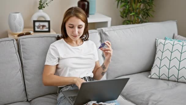 Mladá žena nakupování s notebookem a kreditní kartou sedí na pohovce se zkříženými pažemi gesto doma - Záběry, video