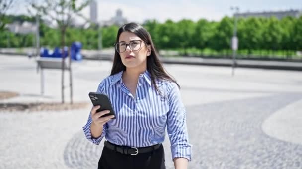 Young beautiful hispanic woman using smartphone walking in the streets of Madrid - Footage, Video