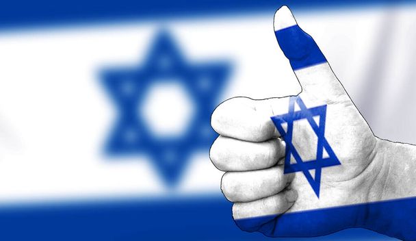 hand with thumbs up in approval with the Israeli flag painted. Image with flag background area out of focus, copy space area - Photo, Image
