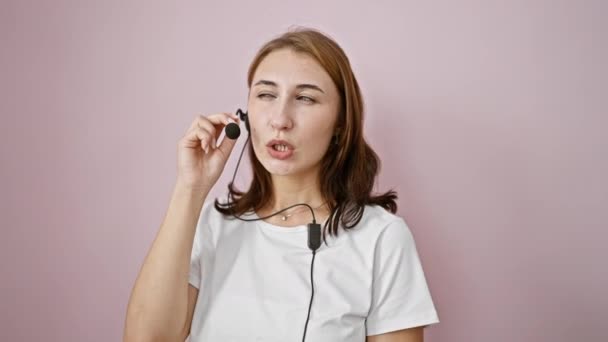 Mujer joven agente del centro de llamadas hablando sobre el fondo rosa aislado - Imágenes, Vídeo