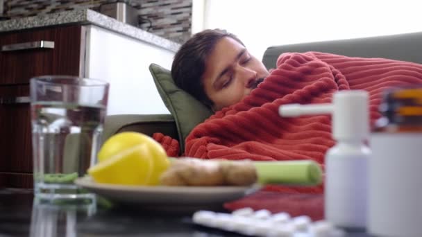 Ingwer, Zitrone, Zwiebeln und verschiedene Medikamente liegen auf dem Tisch des kranken Mannes. Alternativmittel und traditionelle Pillen gegen Erkältungen und Grippe. Kranker Mann in rote Decke gehüllt - Filmmaterial, Video