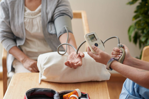 Zbliżenie pielęgniarki sprawdzającej ciśnienie krwi pacjenta ze specjalnym sprzętem medycznym przy stole - Zdjęcie, obraz