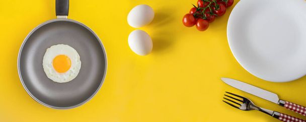Τηγάνι τηγανίσματος με τηγανητό αυγό και υλικά για πρωινό στο κίτρινο φόντο.Copy space. Άνω όψη. - Φωτογραφία, εικόνα