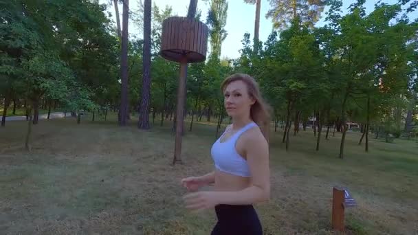 Een atletische vrouw die cardio traint in het park. Joggen is een opwarmertje voor zware lasten. Buiten rennen in het park is gunstig voor vrouwen. - Video