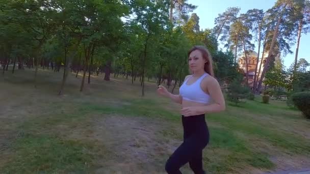 公園のトレーニングカーディオで走る運動女性. ジョギングは重い負荷の前にウォームアップです. 公園で屋外で走ることは女性にとって有益です. - 映像、動画