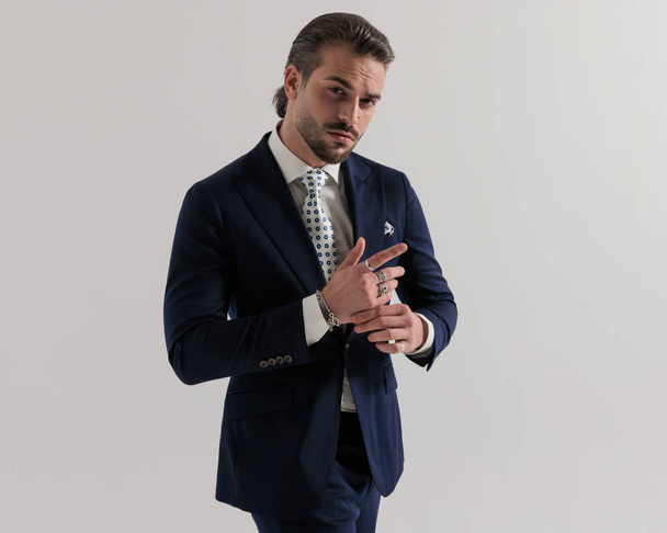 kühler eleganter Geschäftsmann im Anzug, der nach vorne blickt, während er vor grauem Hintergrund die Finger berührt  - Foto, Bild
