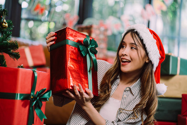 Asiatin mit Weihnachtsgeschenkbox, die in die Kamera lächelt und im Hintergrund jede Menge Geschenkschachteln. Das Mädchen hat aufregenden Ausdruck mit Neujahrsgeschenk Box. - Foto, Bild