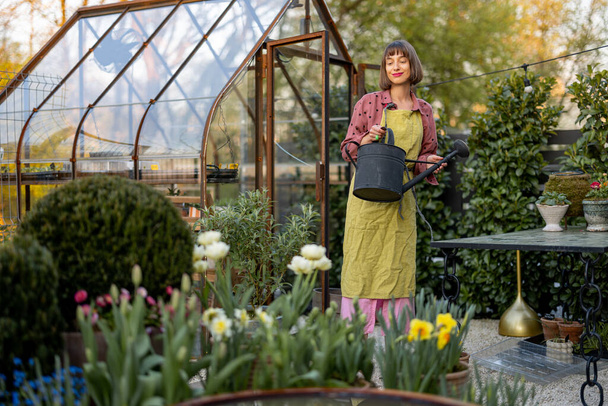 Muotokuva nuori nainen kukkakauppias hoitaa kukkia ja kasveja puutarhassa vintage kasvihuone taustalla. Käsite harrastus ja puutarhanhoito - Valokuva, kuva