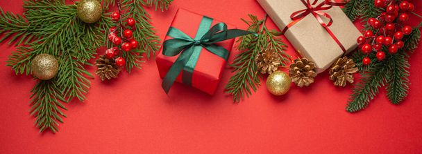 Vánoční nebo novoroční oslava červený papír slavnostní pozadí s dekorací jedle, zabalené dárkové krabice, kornouty, bobule, jiskřivě červené koule. Mezera pro text.. - Fotografie, Obrázek
