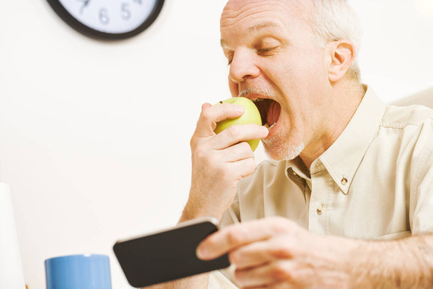 Im Mittelpunkt steht ein grüner Apfel. Während der betagte Schelm jeden Tropfen seiner Vitamine in seiner Küche genießt, erinnert er sich an das Sprichwort und sein Bekenntnis zu Qualitätsfrüchten. - Foto, Bild