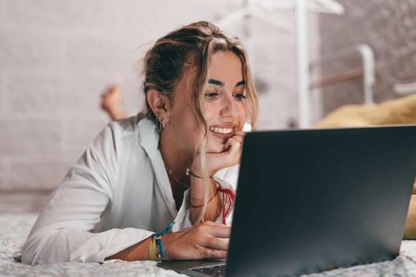 Close-up van een jonge mooie vrouw met behulp van laptop indoor thuis liggen op het bed surfen op het net. Millennial tiener hebben plezier online studeren. - Foto, afbeelding