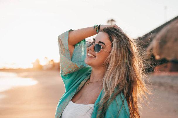 Portret van een jonge vrouw aan het strand die naar de zee kijkt en geniet van vrije tijd en vrijheid buiten. Plezier hebben ontspannen en gelukkige momenten beleven. - Foto, afbeelding