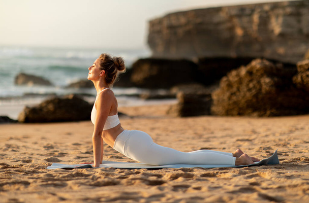 Dama delgada europea joven calma que practica yoga en asana, que hace ejercicio al aire libre en la playa del mar, vista lateral. Estiramientos, deportes, fitness, salud y pilates - Foto, imagen